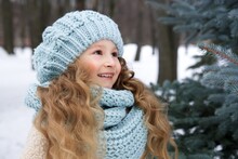 Portrait Of Cute Little Child, Beautiful Kid Girl In Hat And Scarf At Cold Winter Snowy Day Walk In Park And Smile 