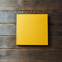 Yellow Hardcover Photobook Isolated On A Wooden Background With Copy Space. Top View, Flat Lay. Blank Closed Book Mockup For Placing Custom Text Or Images. Stylish Wedding Or Family Photo Book.