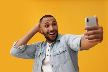 Canvas Print - Smiling young man taking selfie with smartphone on yellow background