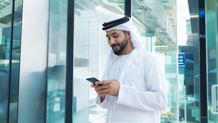 Arab businessman with high-rise buildings with glass windows as background. Arabic Man in Kandura Thobe Thawb for Middle Eastern corporate finance banking concept