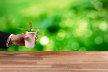 Businessman holding plant pot with his hand promoting forest regeneration and natural awareness. Ethical green business with eco-friendly policy utilizing renewable energy to preserve ecology. Alter