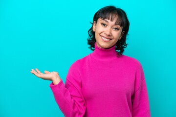 Wall Mural - Young Argentinian woman isolated on blue background holding copyspace imaginary on the palm to insert an ad