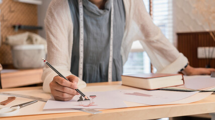 Asian tailor women working to design new fashion collection and sketching model dress in paper