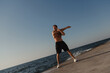 © gstockstudio - Full length of muscular man doing stretching exercises outdoors with the sea on background