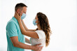© Dorde - Photo of two young apprehensive married people standing face-to-face and holding each other with face masks.