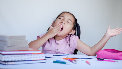 Wall Mural - Portrait Of Sleepy Little Asian Female Child At Desk Tired After Doing School Homework.