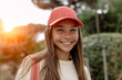 Portrait of beautiful teenage girl (14-15 years old) wearing a pink baseball cap, stands outdoors, sweetly smiling against the backdrop of a sunset.