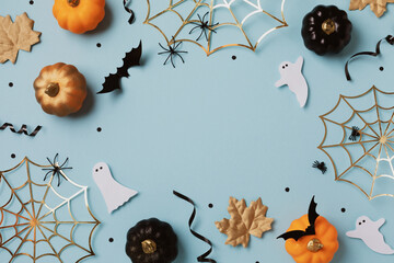 Halloween holiday frame with party decorations from pumpkins, bats, spider web and ghosts top view. Happy halloween greeting card on blue background flat lay style..