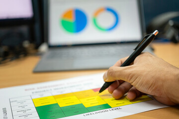 Close-up at the investor hand is using luxury ballpoint pen to write on project investment risk assessment matrix with profit analysis graph in laptop as blurred background. Business work concept.