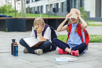 Wall Mural - Schoolchildren are bored reading books and studying homework in school yard. Mental health.