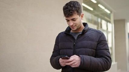 Canvas Print - Young hispanic man using smartphone smiling at street