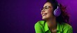 Young girl in green top and glasses enjoying music with headphones isolated on purple background