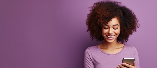 Woman with curly hair happily edits photo from dating app on mobile phone isolated on violet wall