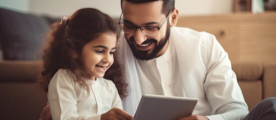 Young Arab father and his adorable daughter enjoying time together at home using a tablet for online shopping