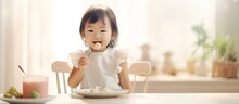 Asian Girl Eating Breakfast At Home With Fork In High Chair