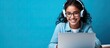 © HN Works - Smiling Indian teen girl using laptop for online study on blue background Happy student in educational webinar