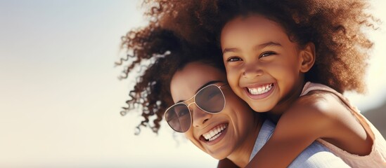 Happy black mother and daughter playing on beach with room for text Sister gives piggyback ride to little girl by the shore Lovely child hugs her mom