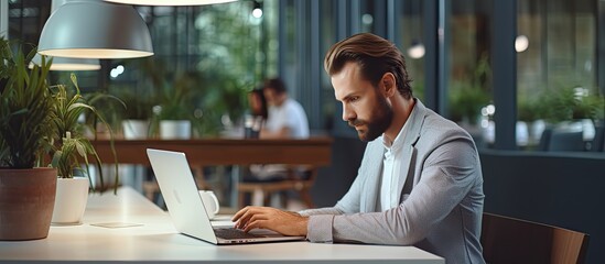 Wall Mural - Attractive businessman using laptop at desk in modern office typing on keyboard