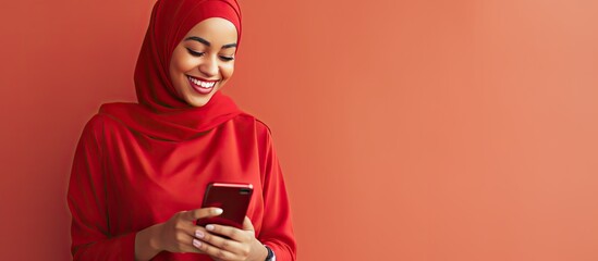 Wall Mural - Young Muslim woman in red headscarf happily using new mobile app in stylish home