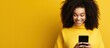 Black girl smiling with smartphone looking at copy space on yellow background