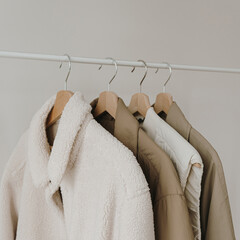 Wall Mural - Autumn outerwear on hanger over white wall. Warm jackets, coats. Aesthetic wardrobe with clothes in neutral colours