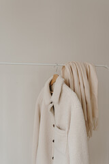 Wall Mural - Autumn outerwear on hanger over white wall. Warm white jacket and skirt. Aesthetic wardrobe with clothes in neutral colours