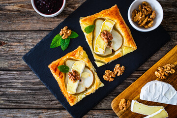 Poster - Baked puff pastry with pear and camembert cheese on baking paper on wooden table
