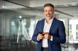 © Stock 4 You - Smiling mature Latin or Indian businessman holding smartphone in office. Middle aged manager using cell phone mobile app. Digital technology application and solutions for business success development.