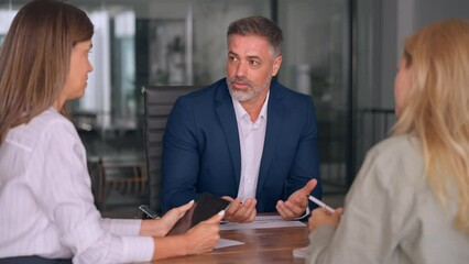 Wall Mural - Group of diverse partners mature Latin business man and European business women discussing project with documents at table in office. Team of colleagues professionals business people working together.