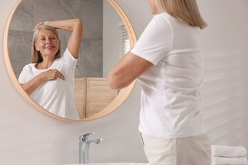 Poster - Beautiful senior woman doing breast self-examination near mirror in bathroom