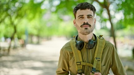 Sticker - Young hispanic man tourist wearing backpack and headphones smiling at park