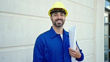 Canvas Print - Young hispanic man worker wearing hardhat holding blueprints at construction place