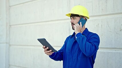 Canvas Print - Young hispanic man worker talking on smartphone using touchpad at construction place