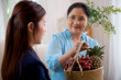 Young asian woman agent insurance visit customer elderly while giving fruit basket in the living room at home, businesswoman or consultant talking and service client with senior, business concept.
