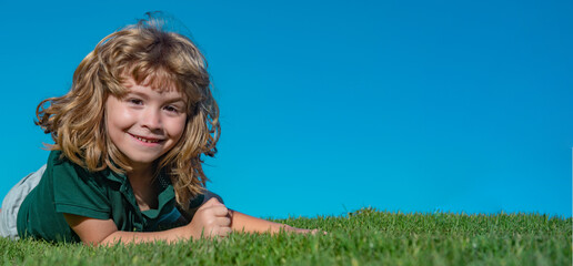 Sticker - Child boy relax outdoors in sunny summer day. Happy child laying on green grass. Funny kid outdoor in spring garden. Spring and kid. Wide photo banner for website header.