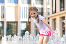 Active Little Girl Playing With Splash Spray Water. Happy Kid In Fountain In Wet Clothes. Summer Children Pastime, Entertainment, Recreation. Child's Leisure, Childhood In City