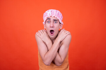 Wall Mural - Funny guy in a pink cap poses on an orange background and washes in the shower.