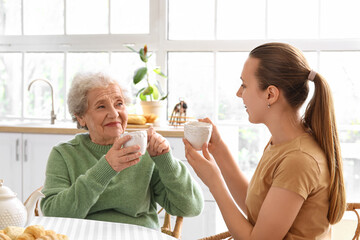 Wall Mural - Senior woman with her granddaughter drinking tea in kitchen