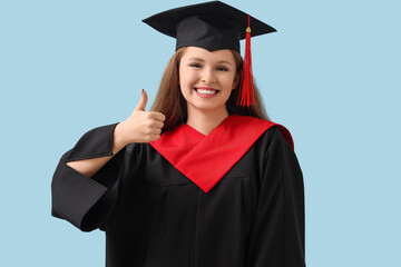 Wall Mural - Female graduate student showing thumb-up on blue background