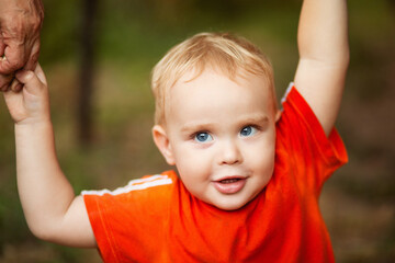 Wall Mural - portrait of small blond boy walking in park with parents and holding their hands. Concept of happy family and childhood