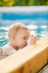 Portrait of small red-haired boy bathes in pool with hand support, baby swimming in water, summer leisure