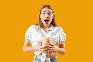 Beautiful shocked young woman with pack of french fries on yellow background