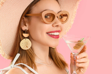 Wall Mural - Beautiful young woman in wicker hat with glass of martini on pink background