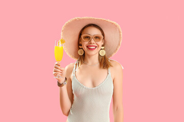 Wall Mural - Beautiful young woman in wicker hat with glass of tasty citrus cocktail on pink background