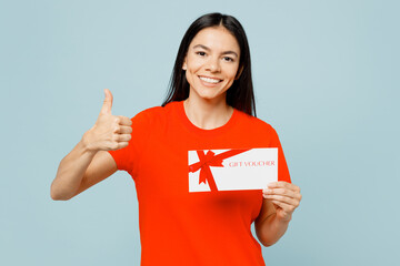 Wall Mural - Young latin woman wear orange red t-shirt casual clothes hold gift certificate coupon voucher card for store show thumb up isolated on plain pastel light blue cyan background studio Lifestyle concept