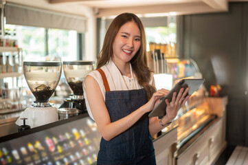 An Asian woman entrepreneur using tablet checking stock or sale income in modern coffee shop , concept small business