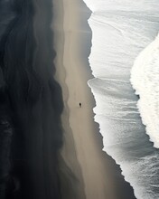 Aerial Shot Of A Distant Person Walking On The Black Sands Beach With Snow White Ocean Waves. Gravity Defying Northern Sea Winter Landscape.
