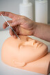 a cosmetologist trains to inject a cosmetic syringe into the face of a rubber mannequin