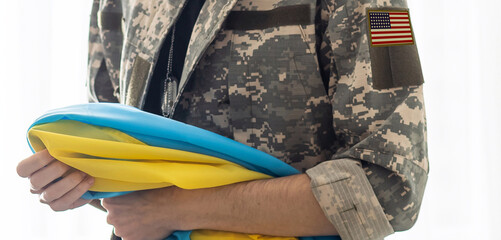 Wall Mural - American Flag on Soldiers arm and flag of the Ukraine at background. US military support Ukraine