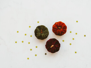 Autumn composition with various colors velvet pumpkins and confetti stars on white background.